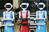 Three robots with trays, dressed in blue and red aprons, standing inside Nairobi's Robot Café