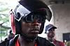 A close-up photo of a motorcycle rider wearing a helmet and dark shades in Karimah Ashadu\u2019s \u2018Machine Boys\u2019 film.