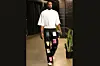 NBA player Precious Achiuwa pictured mid-walk while wearing patchwork black pants and a white tee.