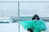 Eshete stands in front of a chain link fence, he is wrapped in large plastic sheets while it snows.