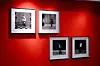 Four black-and-white photographs are framed and displayed on a vivid red wall. Each photo captures a stylish portrait of an individual standing or posing against bold, patterned backdrops, evoking a retro or studio aesthetic. The arrangement and contrast highlight African identity and vintage visual culture.
