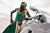 Black Sherif, dressed in green garments, poses on a motorbike.