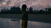 A film still from Baba of a young boy standing near a lake.