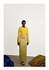 A model poses for a photo in an ankle-length yellow dress made with Aso Oke fabric.