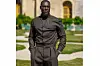 \u200bStormzy wears a dark olive green wool ensemble composed of a pointed-collar shirt with hidden buttons and matching wide-leg trousers, a silver wristwatch, and a clean-shaven look