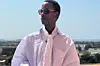 Senegalese filmmaker Moe Sow posing for a picture in a white tunic-like outfit with a skyline behind him.