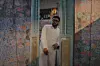Soulja standing inside a green door frame, rapping. To his left and right are colorful walls with flower print.