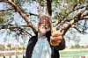 A photo of Nazeem Randera under a tree, pointing his marked thumb to the camera after casting his vote.
