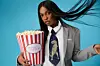 Actress Efe Irele flips her hair mid-pose while wearing a blazer and carrying a bag of popcorn.