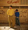 Ahmed Atef and Mohamed Tarek are wearing tight yellow and blue shirts with wide pants held by golden statement belts, looking straight at the camera. Above them, Arabic letters say \u201cEgyptian.\u201d