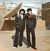 Ahmed Atef and Mohamed Tarek are posing together on a Cairene rooftop next to a large satellite dish, wearing black suits and, respectively, white and red shoes that complement their respective white and red shirts.