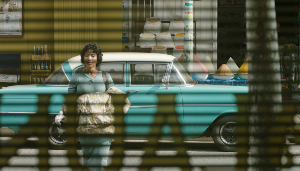 “1968 marks the end of the sixties and heralds the beginning of the seventies, and to me that was a pivotal time in South African history.” - Zamo Mkhwanazi. A still from Zamo Mkhwanazi’s ‘Laundry’ showing a woman carrying a folded blanket while crossing the road. Behind her is a car parked in front of some shops selling food items.
