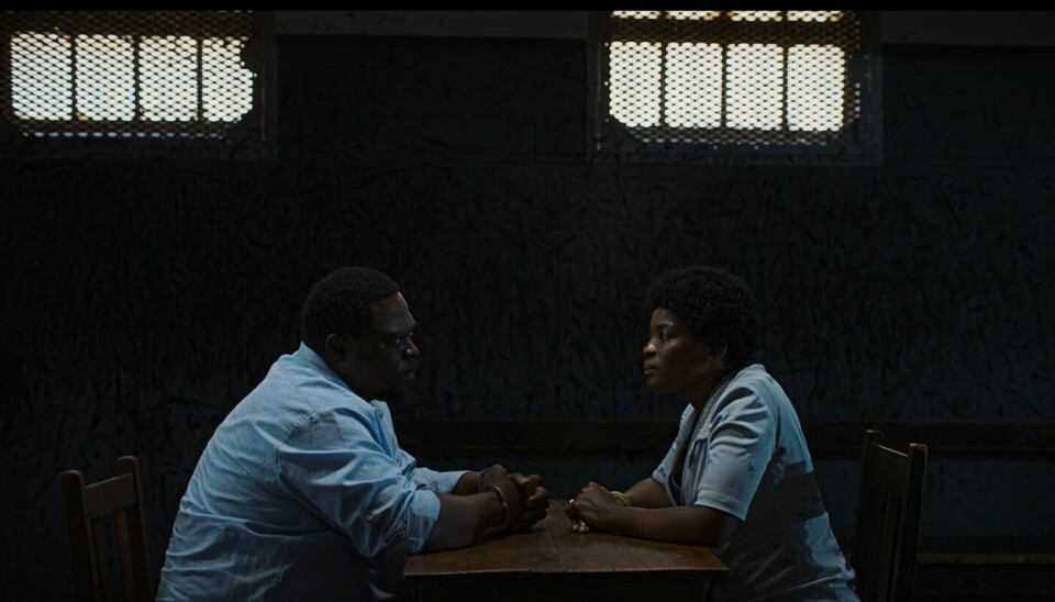 “The film is inspired by something that happened to my mother’s family. My grandfather owned a laundry and in 1954, about six years into the apartheid government, the business was taken from him and he lost his livelihood.” - Zamo Mkhwanazi. A still from Zamo Mkhwanazi’s ‘Laundry’ showing a man wearing a light blue shirt and in cuffs sitting across the table from a woman also in a light blue patterned top and full hair.