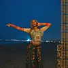 A promo photo of Osé for her latest single “24HRS” showing her in a patterned top and plaid pants by the beach.