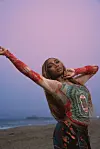Osé poses at the beach wearing a patterned top and brown braided hair.