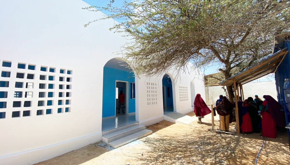 A maternity ward in Mogadishu, Somalia, designed by architect Omar Degan. White and blue maternity ward building in Mogadishu, Somalia, designed by Omar Degan. The structure features arched doorways and perforated walls for ventilation, with women gathered outside under a tree.