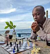 A photo of a man seated by the beach looking at a chessboard.