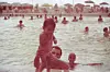 Old sepia image of a man in a public swimming pool, holding a toddler who is standing by the edge of the pool. Behind him is a young, laughing girl.