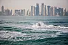 View of Doha’s highrises from the sea. Two people are jet skiing on the water.