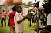 Akinola Davies Jr. sits behind a camera and talks to a young boy.