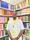 A picture of Taiwo Hassan standing in front of a bookshelf.
