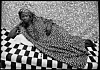 A woman with a headdress on is lying with her body turned towards the camera on a black and white-checked lounger.