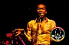Fela performing on stage with a golden striped shirt.