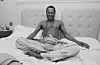 Fela Kuti poses for a photo on a bet with his saxophone on his lap.