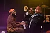Nduduzo Makhathini sits at a piano, laughing as he watches Wynton Marsalis playing the trumpet.