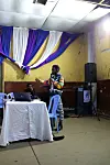 Nick Wambugu stands beside a table with a laptop, holding a microphone while speaking to attendees during a cinematography workshop at Kaloleni Social Hall.