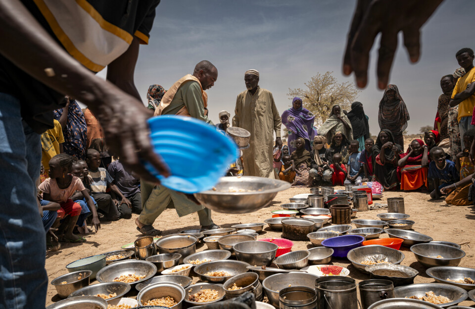 Sudanese refugees from Zamzam camp outside of El Fasher, in Darfur, receive food at an Emergency Response Room Communal Kitchen. The UN warns that thousands of children in El Fasher are at imminent risk of famine death. A group of people sit and stand around bowls and pots of food.