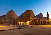 Men in white jalayib are kneeling in front of a mosque by the mountains in Kassala, praying as the sun sets.