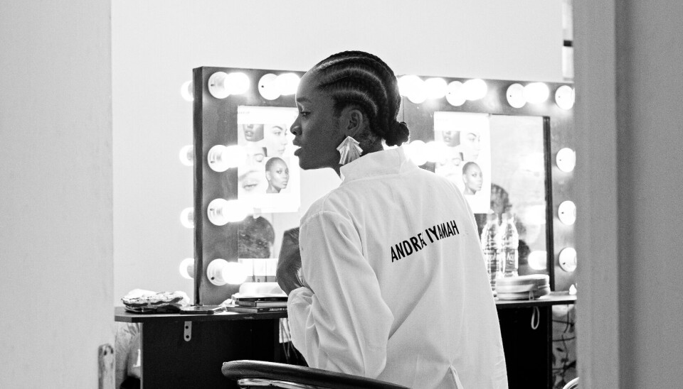 The book captures the restlessness, excitement, chaos, conflict, and apprehension that go into bringing a fashion show to life. A black and white image of a model in the dressing of an Aindrea Iyama fashion show.