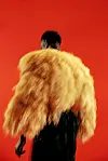 A blurry shot of a man wearing a feather jacket in front of a red background
