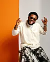 Tim Godfrey wears a casual outfit, posing over a white and orange background