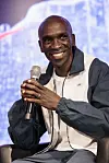 A close-up of Eliud Kipchoge smiling with a microphone in his hand.