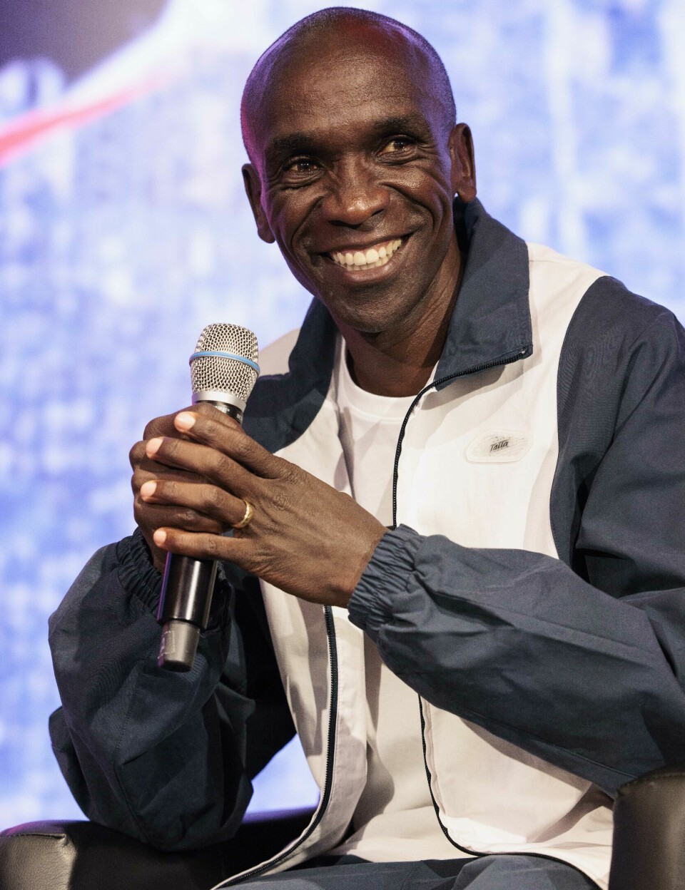 Eliud Kipchoge’s next plans include a world tour of completing a marathon on every continent. A close-up of Eliud Kipchoge smiling with a microphone in his hand.