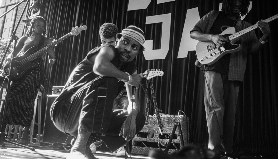 Lerato Orchestral Collective performing at Kids Love Jazz An image of the frontman for Lerato Orchestral Collective on stage during Kids Love Jazz. He is crouching, looking at the audience, with other members of the band behind him.