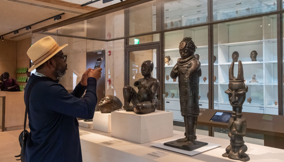 Guests view artworks at the opening of the Imaginary Exhibition: Homecoming at MOWAA in Benin City, Edo State, Nigeria, on November 9, 2025. A man wearing a hat stands in front of sculptures at the MOWAA gallery in Benin, photographing them.