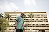 A photo of Ata Kak wearing an African print shirt with a large, block building behind him.
