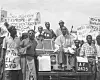 A bespectacled man in batakari (woven smock) with a smoking pipe in his mouth sits on the bonnet of a Land Rover during a protest by Ghanaians against the decision by the French government to conduct nuclear tests in Algeria.