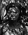Portrait of a woman at a funeral in southern Ghana. She wears a dark duku (headscarf) and an Adinkra wax print cloth.