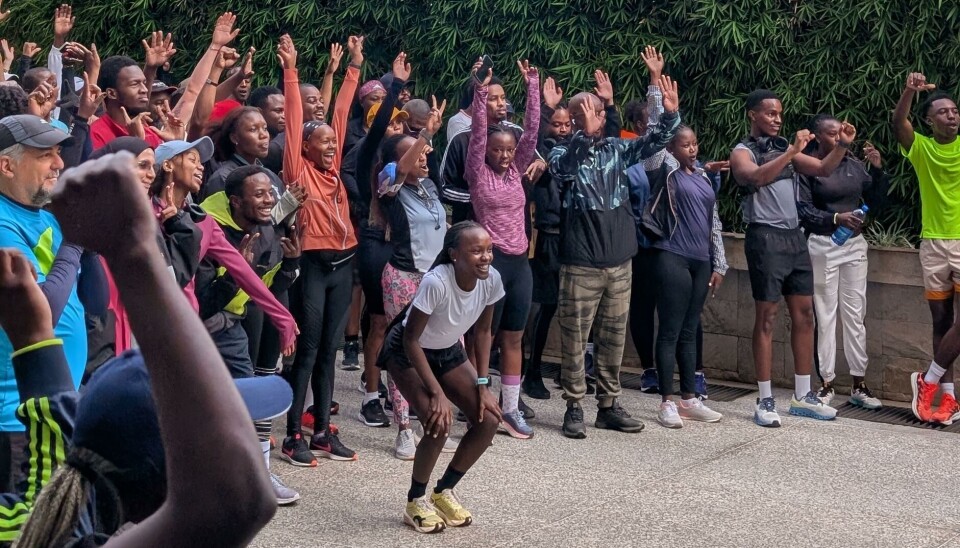 We Run Nairobi members pose and cheer for a photo before setting off on their weekend run. Emily Chepkor crouches in front of a group of runners as they pose for a photo.