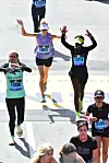 Emily Chepkor crosses a blue and yellow finish line at the 2022 Boston Marathon next to other finishers