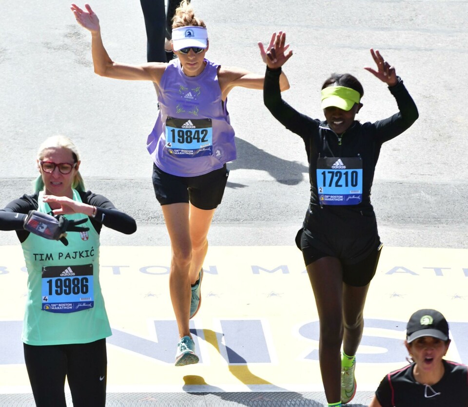 Emily Chepkor crosses the iconic blue and yellow finish line at the 2022 Boston Marathon. Emily Chepkor crosses a blue and yellow finish line at the 2022 Boston Marathon next to other finishers