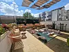 A rooftop terrace with floor cushions, rugs, plants, and casual seating under a shaded canopy.