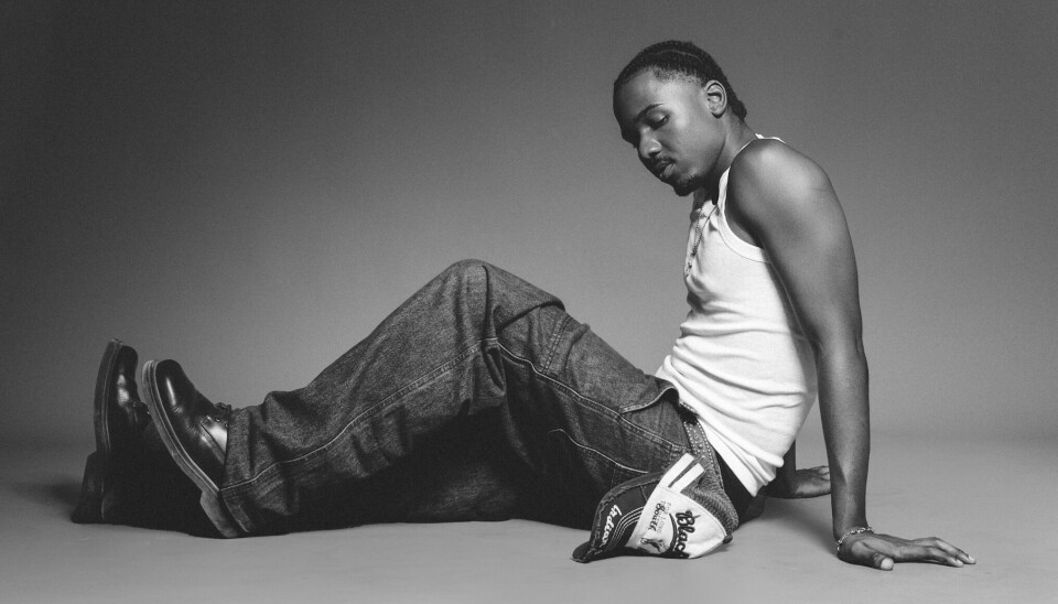 I wanted it to be digestible, especially for someone hearing me for the first time,” Itare says of his EP. “Especially from Tanzania.” Black and white portrait of Tanzanian artist Itaré in a white tank top, looking downward.
