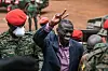 Uganda's veteran opposition figure Kizza Besigye, surrounded by men dressed in military gear, smiles and gestures as he arrives at the Makindye Martial Court in Kampala.