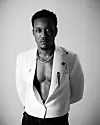 Black-and-white portrait of Rwandese artist and producer Element Eleéeh wearing a white blazer with his chest showing.