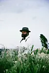 A promo image of Sjava for his new album, iNkanyezi NeZinkanyezi. He is in a field, surrounded by lush greenery. He wears a grey hat and a white shirt.